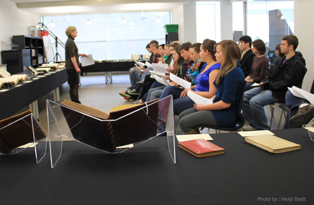Curator, Luise Poulton, and students from Professor Ann Engar's Honors ITW course, Spring Semester 2011. A group of students listens to a lecture while rare books are displayed in the foreground. Photo by Heidi Brett