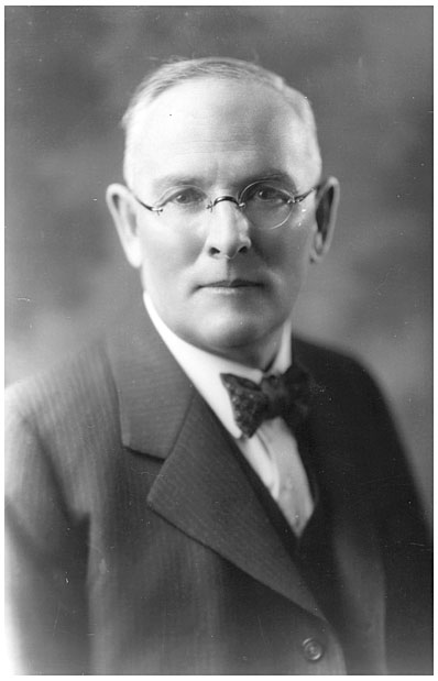 A portrait of an elderly man in a dark suit and bowtie, with a blurred background, evoking a vintage, formal aesthetic.