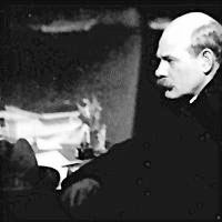 A man sitting at a desk, surrounded by papers and books, in a dimly lit room, conveying a serious and contemplative atmosphere.