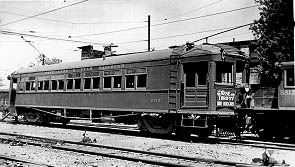 A vintage black-and-white photo of an electric train car parked on the tracks, showcasing its windows and classic design.