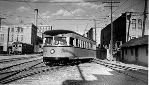 A vintage streetcar maneuvering through railway tracks, surrounded by urban buildings and telephone poles on a cloudy day.