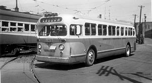A vintage city bus in black and white, marked "Lagoon," turns onto a street near a parked train, showcasing mid-20th century transportation.