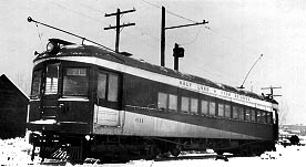 Black and white image of an old electric train car, partially snow-covered, next to utility poles and a signal.